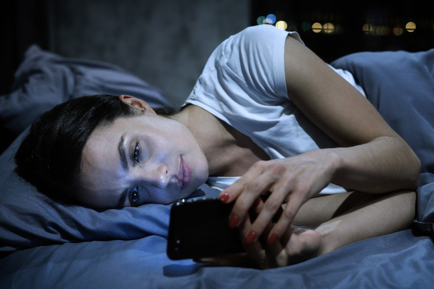 Zdjęcie przedstawia dziewczynę, która patrzy się w ekran telefonu przed snem.